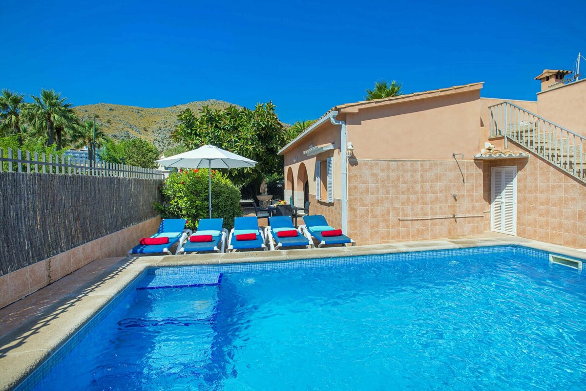 A swimming pool with blue chairs and an umbrella in front of a house