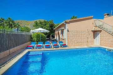 A swimming pool with blue chairs and an umbrella in front of a house
