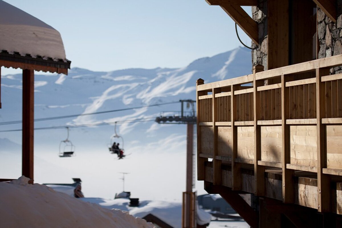 A ski lift is visible in the distance behind a wooden balcony