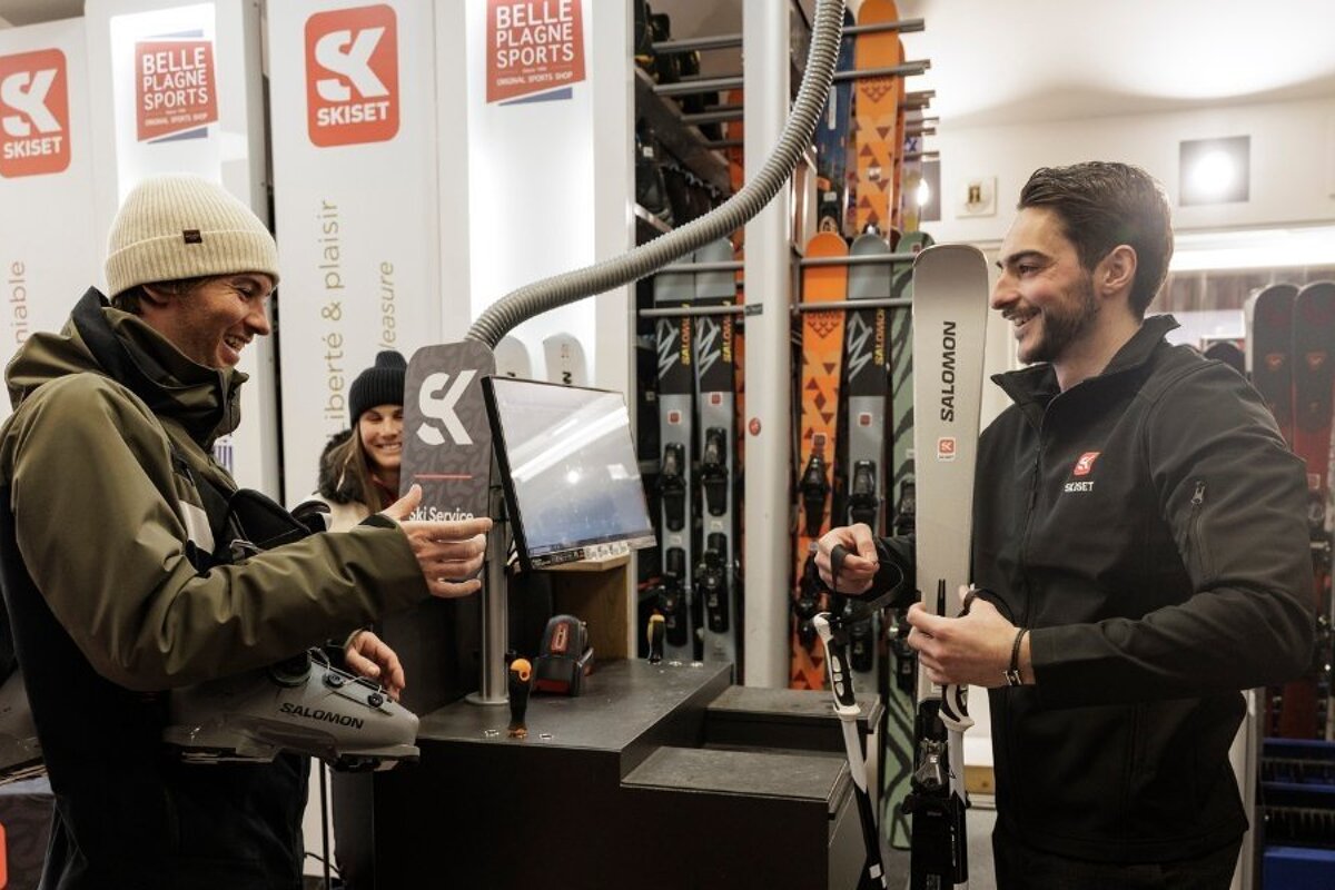 Customers smiling while renting ski boots and Salomon skis from an employee in a Skiset rental shop.