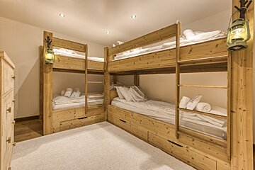 Cozy room with L-shaped, natural wood bunk beds featuring white bedding and rustic lantern lights, set on a plush white carpet.