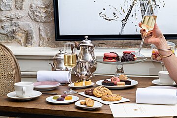 A woman holds a glass of champagne in front of a table full of desserts