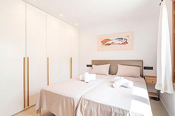 Bright bedroom featuring two beds, white built-in wardrobes with wooden handles, a colorful abstract artwork above the headboard, and natural light.