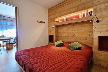 A bedroom with a red bed and a wooden wall