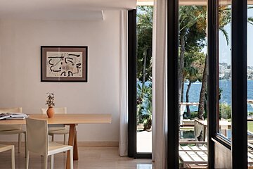 A modern dining room with abstract art, large windows overlooking a beautiful sea view with palm trees and a distant city skyline.