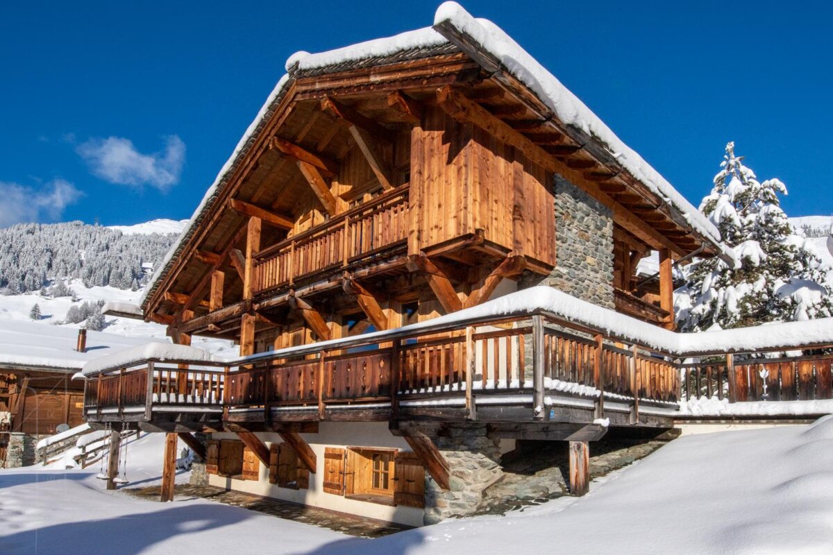 A large wooden house covered in snow with a blue sky in the background