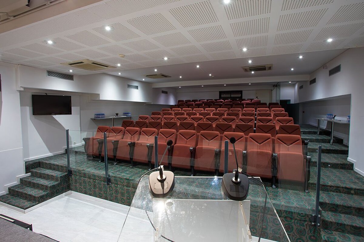 A large auditorium with red chairs and two microphones