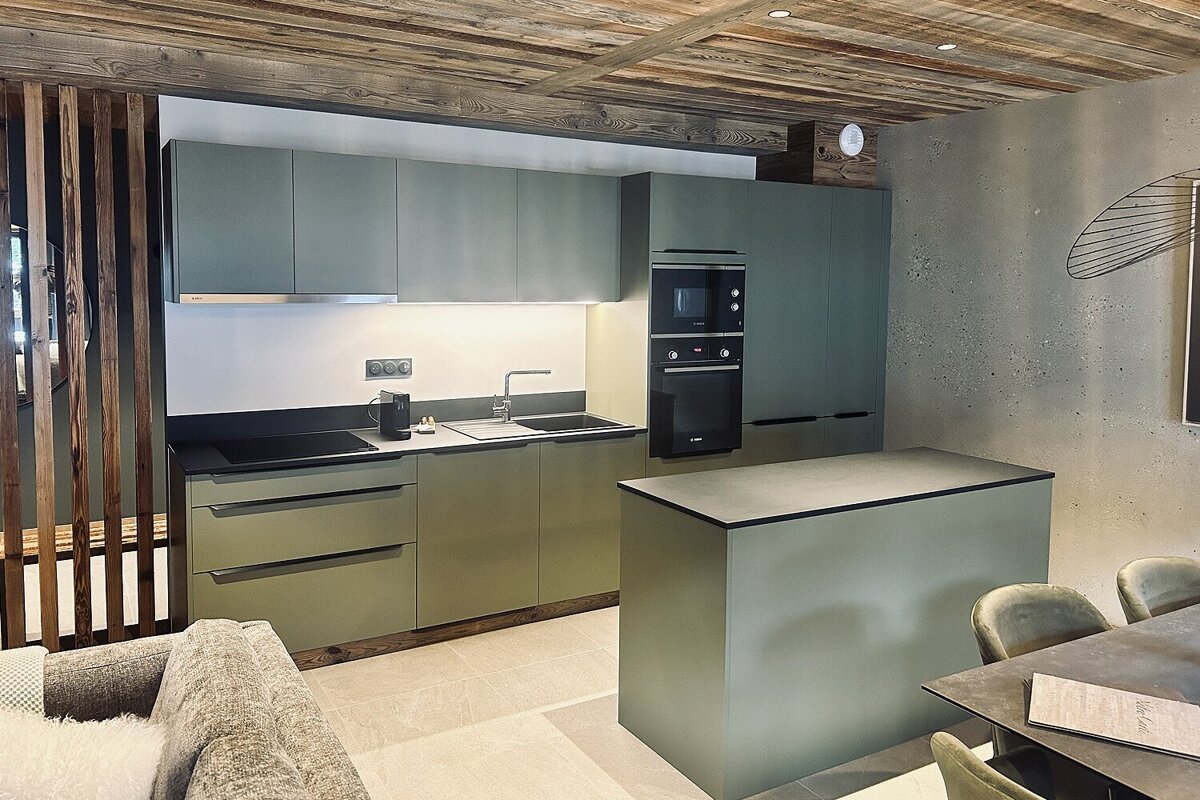 Chic sage green kitchen with a central island, integrated appliances, and a rustic wooden ceiling.