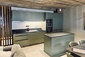 Chic sage green kitchen with a central island, integrated appliances, and a rustic wooden ceiling.