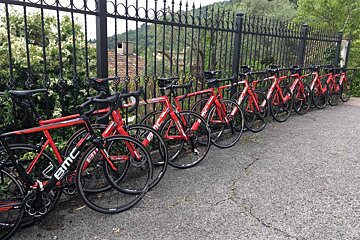 A row of red bmc bikes are parked in front of a fence