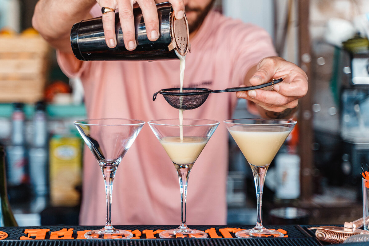 A bartender pours a drink into a martini glass
