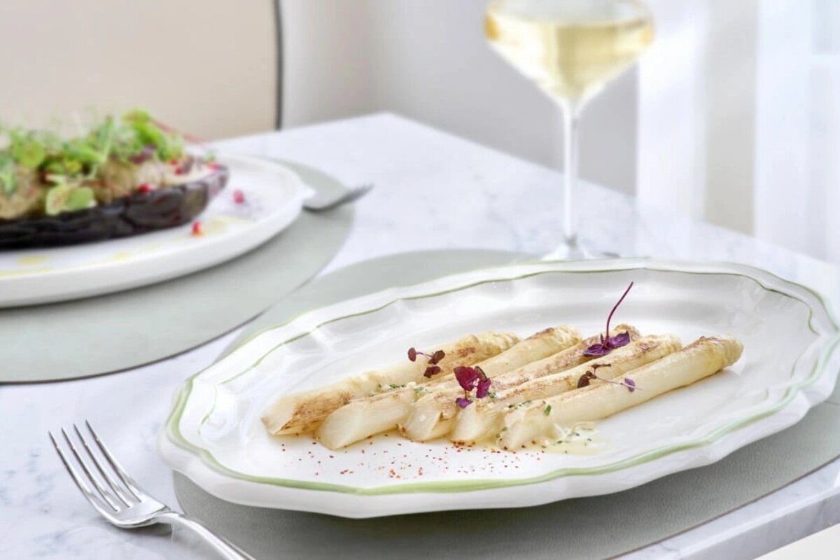 A plate of asparagus sits on a table next to a glass of wine