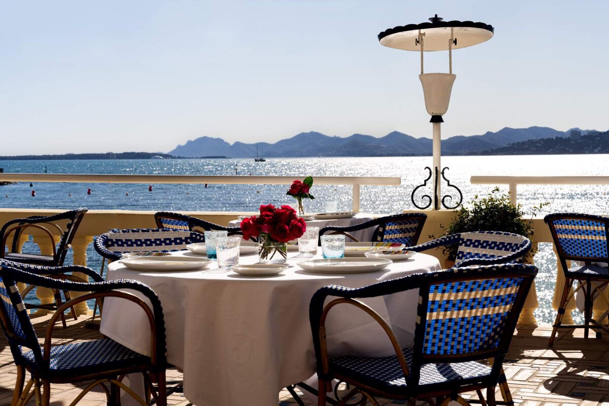 A table with a white table cloth and blue chairs overlooking the ocean