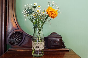 A bottle with flowers in it has a lace ribbon around it
