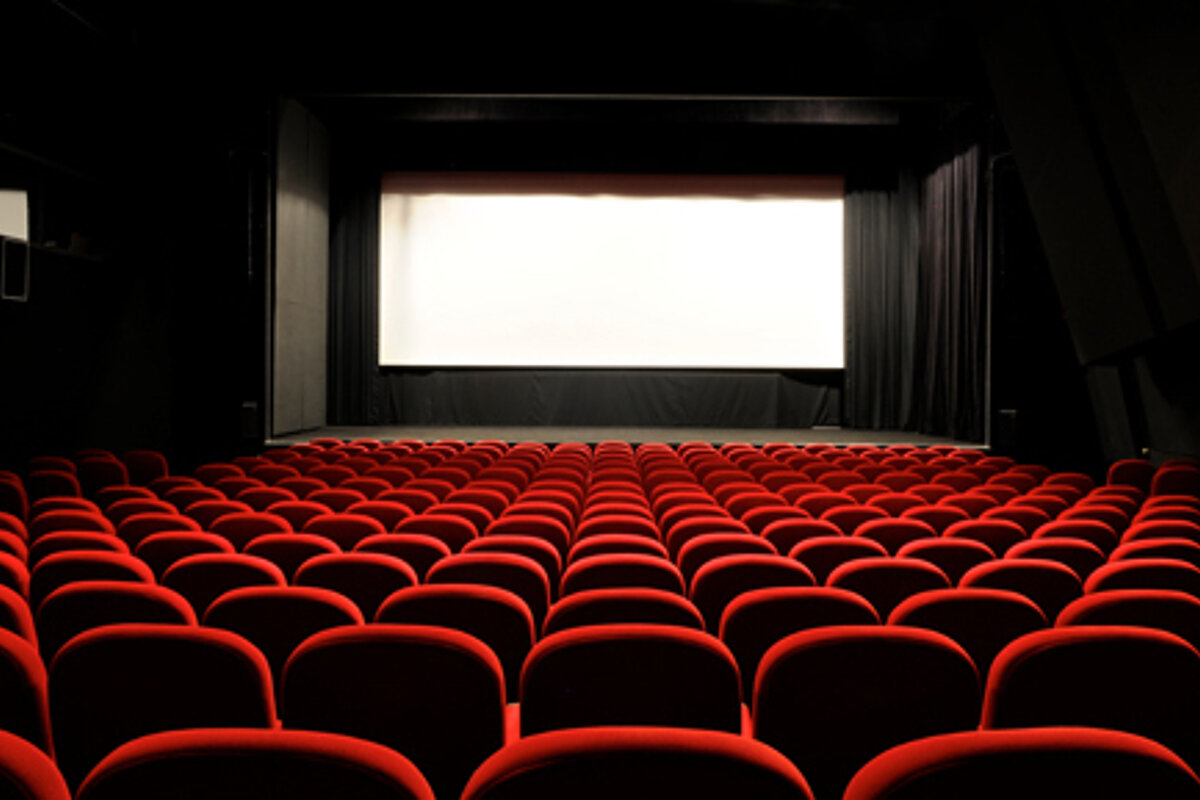 An empty movie theater with red seats and a white screen