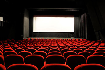 An empty movie theater with red seats and a white screen
