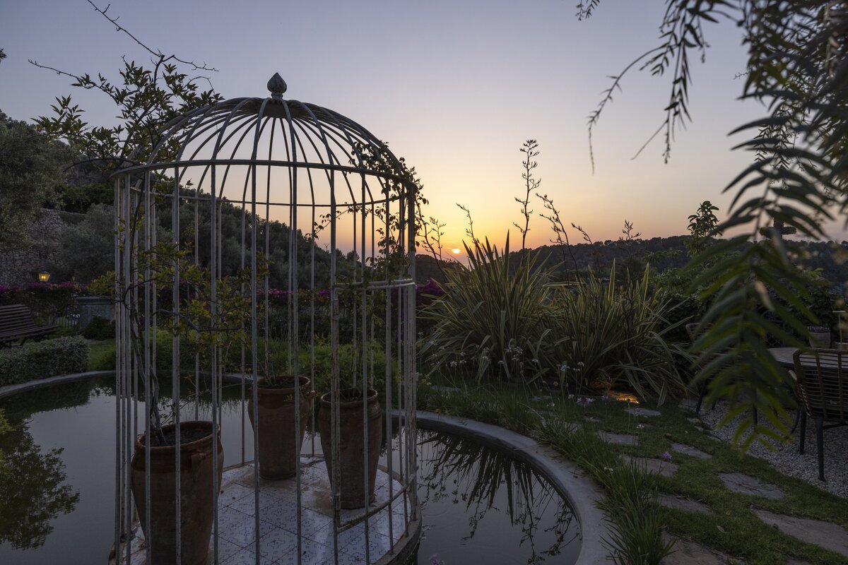 A bird cage in a garden with a sunset in the background