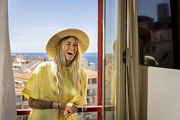 A woman wearing a straw hat and a yellow shirt is standing on a balcony