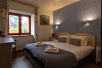 A cozy bedroom with a large bed, textured blue accent wall, and a wooden window framing a lush mountain view.