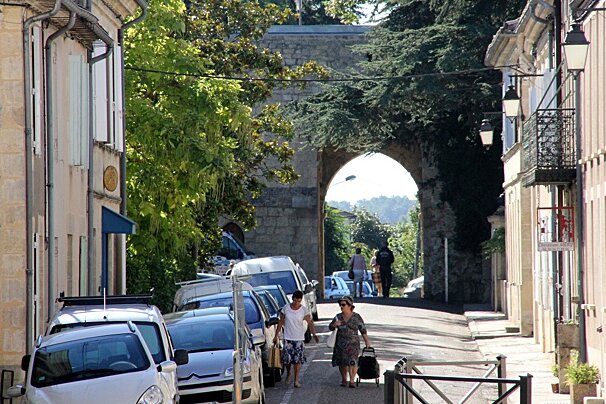 2 people walking down the street with an ancient wal in the back