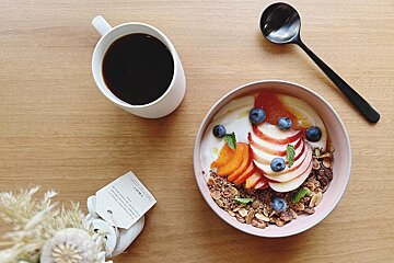 A bowl of granola with fruit and yogurt next to a cup of coffee