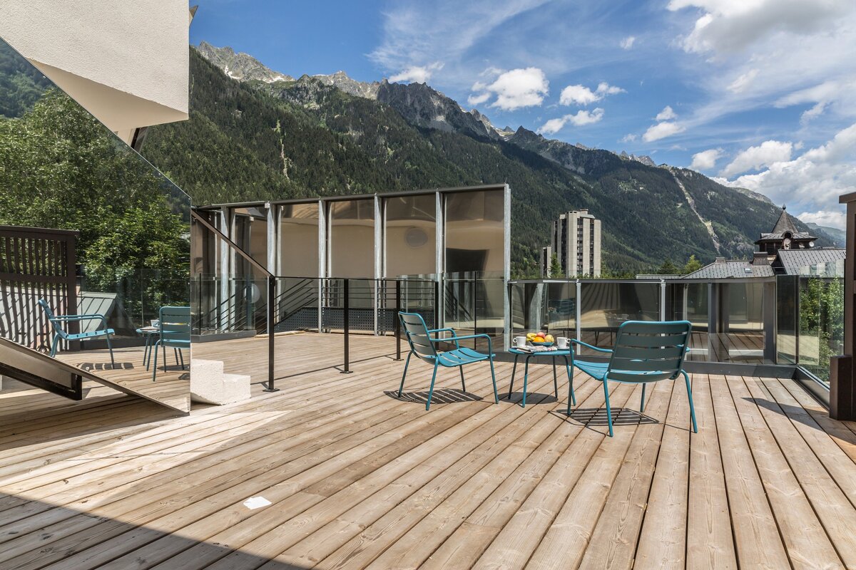 A balcony with chairs and a table with mountains in the background