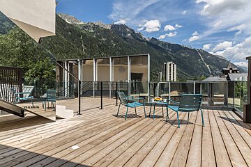 A balcony with chairs and a table with mountains in the background