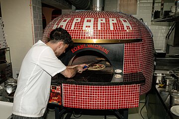 A man is putting a pizza into a red oven that says forni valoriani