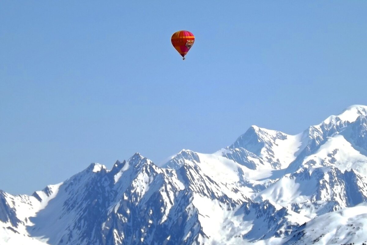 a red hot air balloon above snow capped mountains