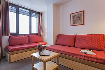A living room with a red couch and a laptop on a table