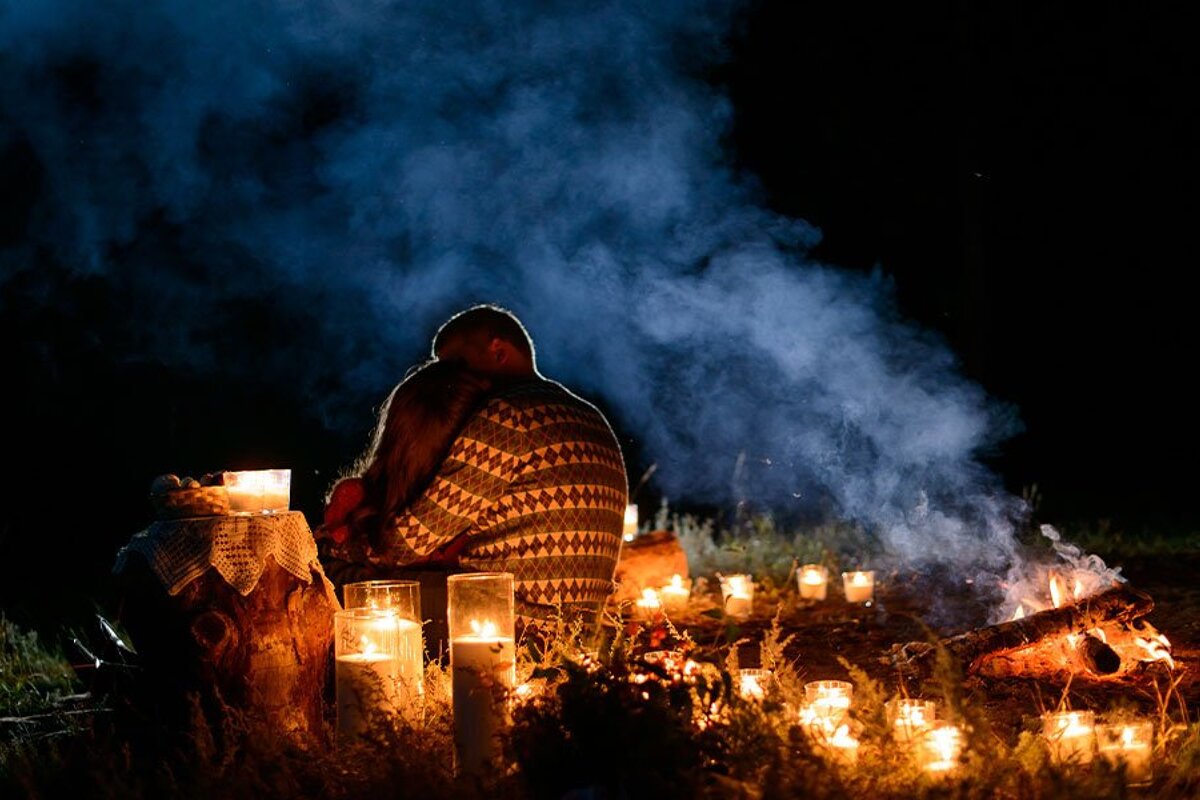 A couple sits in front of a fire surrounded by candles