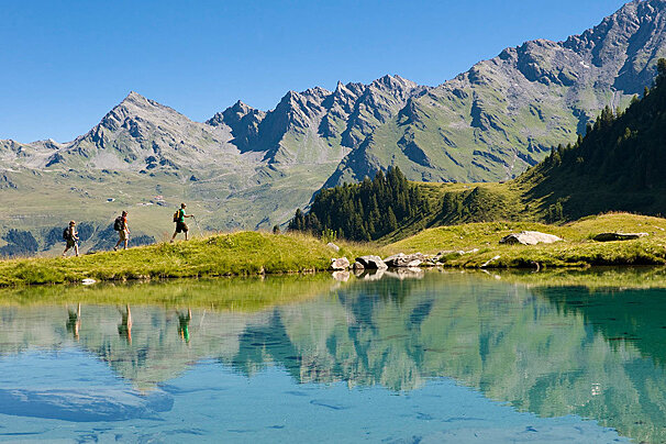 A couple of people walking across a lake with mountains in the background