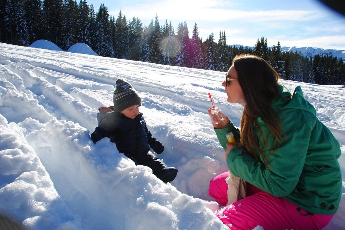 A woman blowing soap bubbles next to a child in the snow