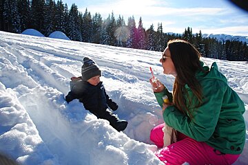 A woman blowing soap bubbles next to a child in the snow
