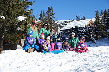 A group of children are sitting in the snow wearing purple shirts that say 