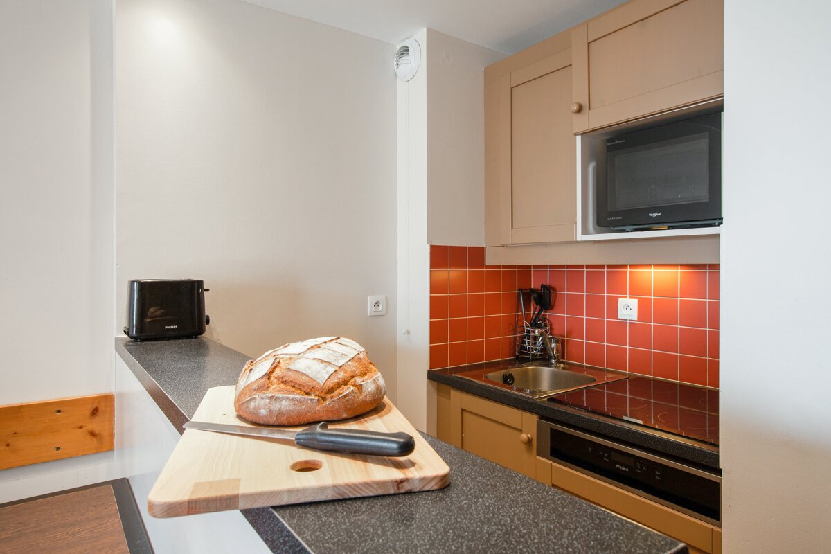 A kitchen with a toaster and a microwave and a loaf of bread on a cutting board