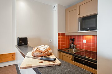 A kitchen with a toaster and a microwave and a loaf of bread on a cutting board