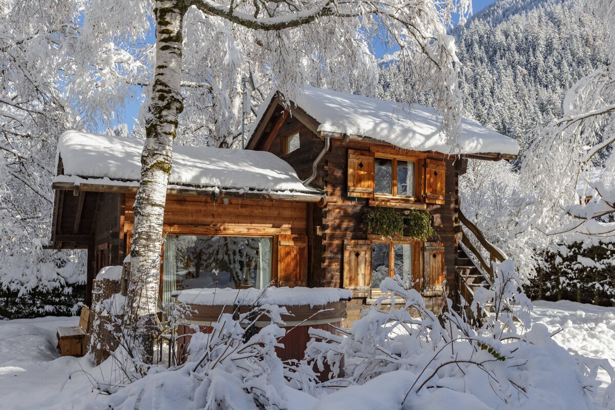 A small wooden cabin is surrounded by snow covered trees