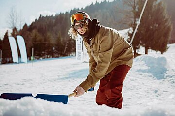 a man with a shovel re-shaping a snowboard jump