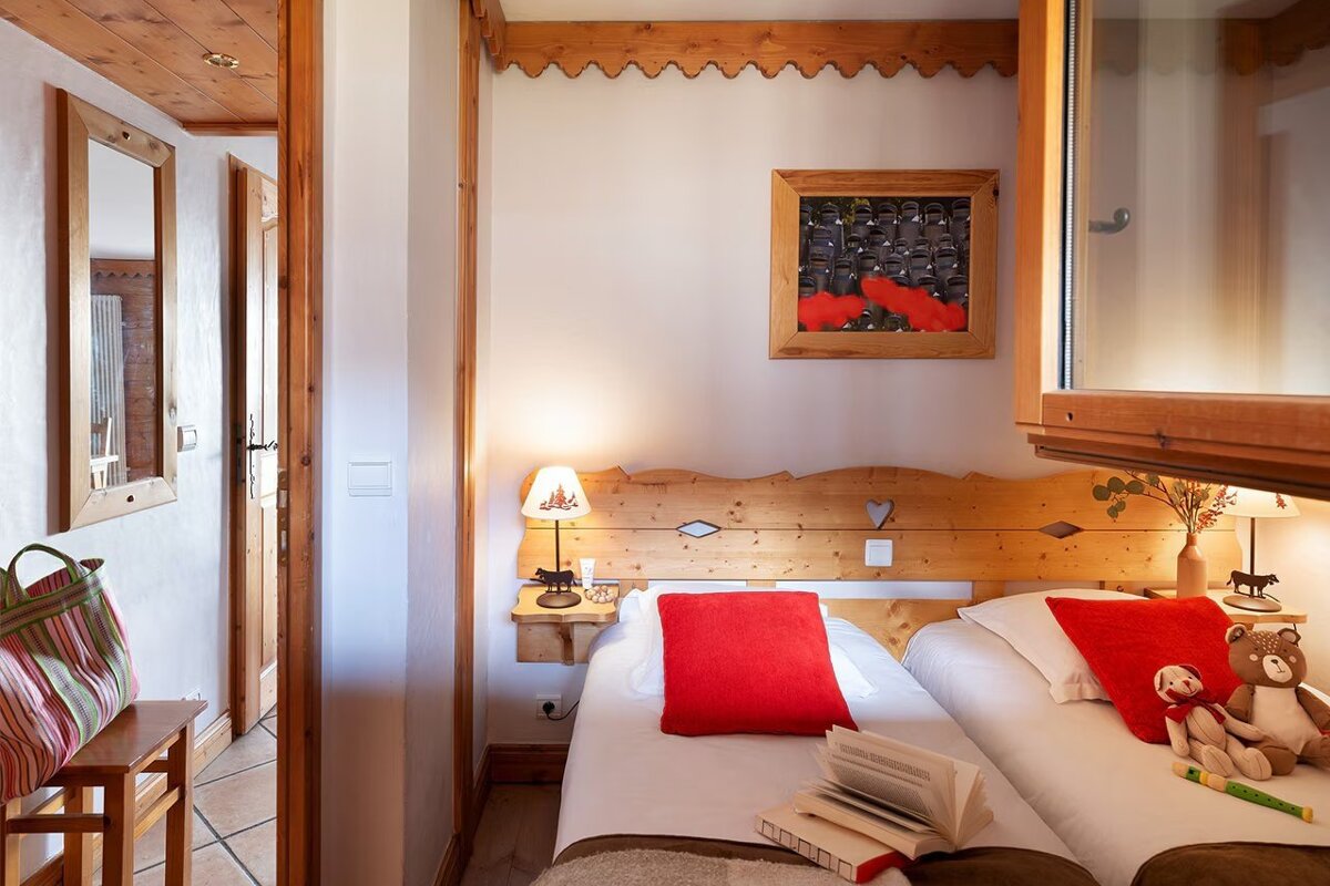 Cozy chalet-style bedroom with twin beds, red accent pillows, and rustic wooden details.
