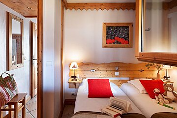 Cozy chalet-style bedroom with twin beds, red accent pillows, and rustic wooden details.