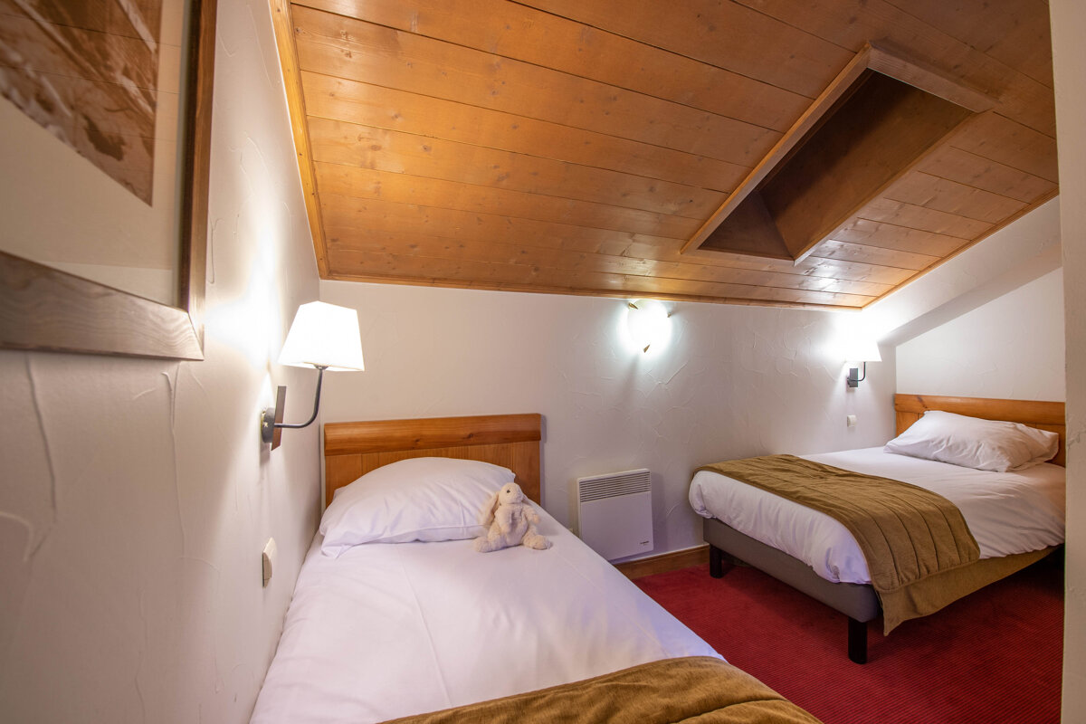 A bedroom with two beds and a lamp on the wall