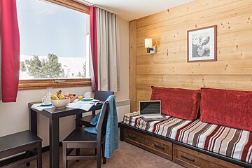 A room with a table and chairs and a laptop on the couch