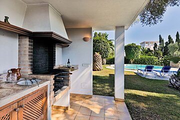 A patio with a barbecue and a pool in the background