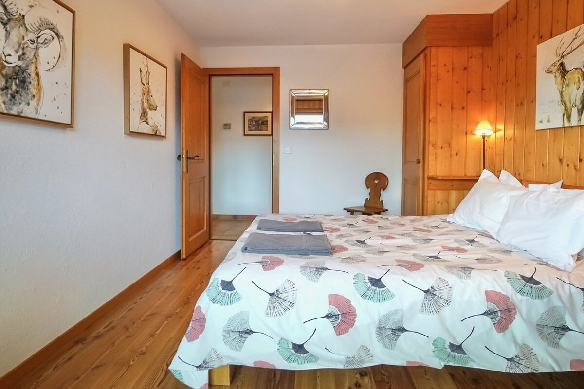 A cozy bedroom with wooden floors, white walls, and wood paneling. A bed with a fan-patterned duvet, animal artwork, and an open door.