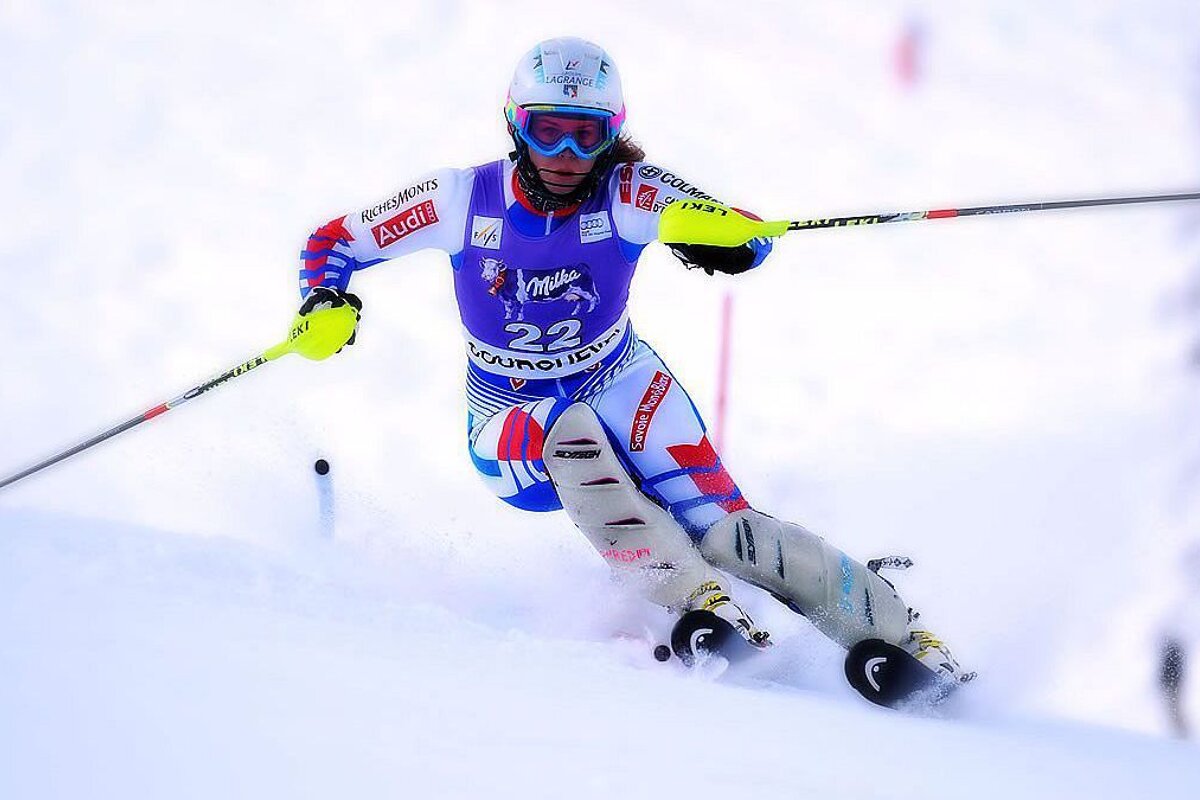 A skier wearing a milka uniform is skiing down a snowy slope