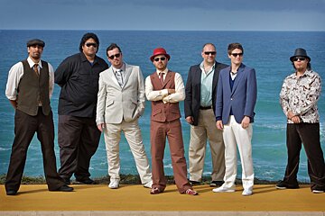 A band standing in front of the ocean, Fat freddy's drop