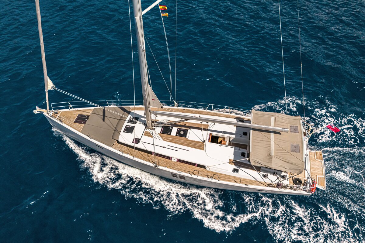 An aerial view of a white sailboat with a wooden deck cruising through deep blue ocean waters.
