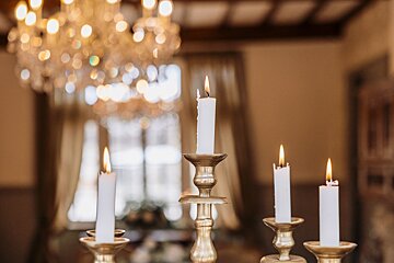 Candles are lit in gold candle holders in front of a chandelier