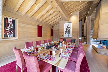 A dining room with a long table and pink chairs